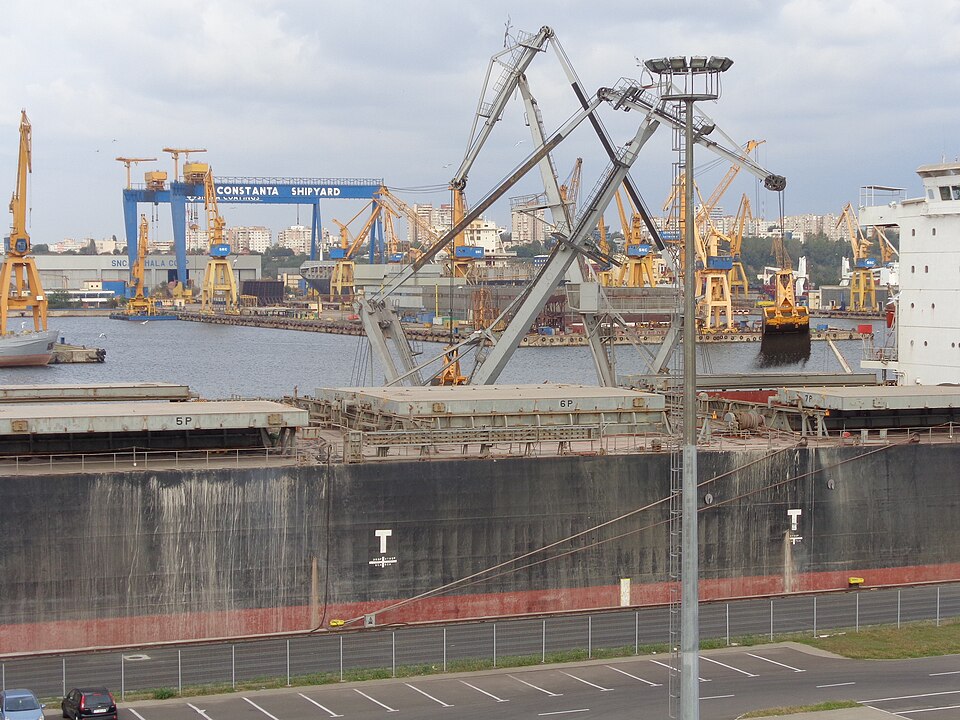 A bulk carrier loading coal at the Port of Constanța, with cranes and the Constanța shipyard behind