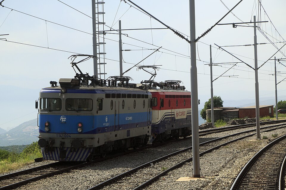 Two HŽ Cargo electric locomotives running downhill through Meja station on the Zagreb–Rijeka line
